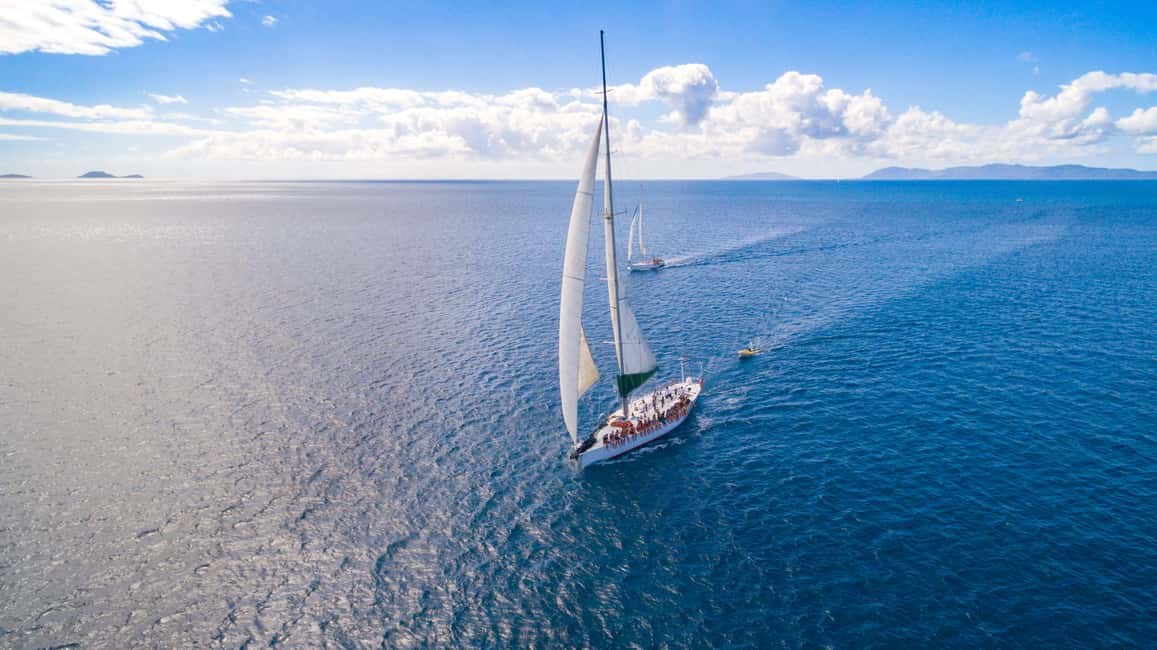 A sailboat heeling across open blue water, islands low on the horizon