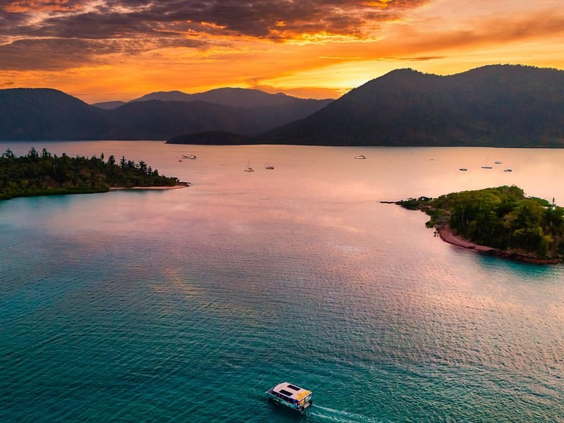 Sunset over the Whitsunday Islands from the air, a small boat crossing the still water between two islets