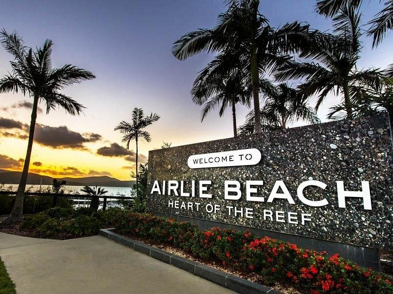 The Welcome to Airlie Beach sign at dusk, palms and flower beds around it