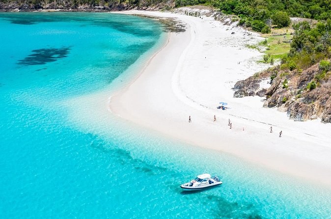 A white sand spit curling into turquoise water below a wooded headland, a motorboat at anchor off the point