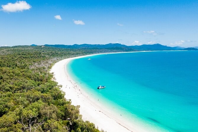 The long white curve of Whitehaven Beach seen from above the forest, one boat anchored in the shallows
